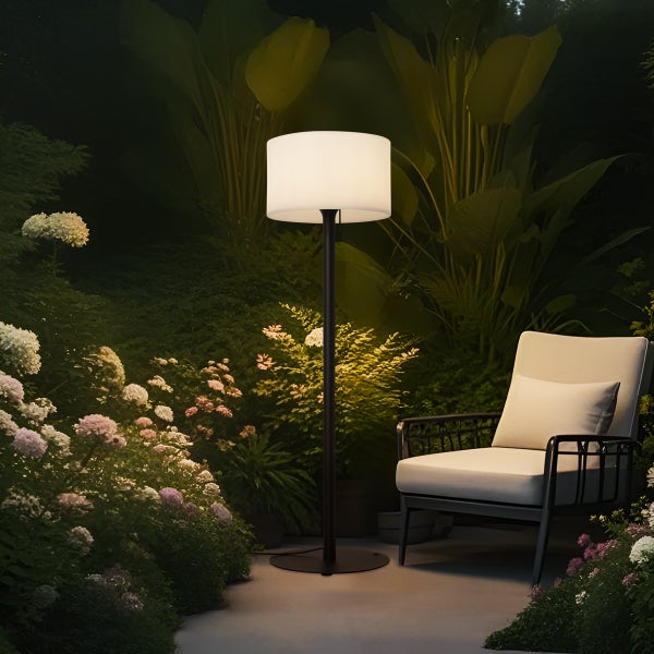 Moderne Außenstehleuchte mit weißem Schirm und schwarzem Gestell in einem nächtlichen Garten neben einem Gartenstuhl.