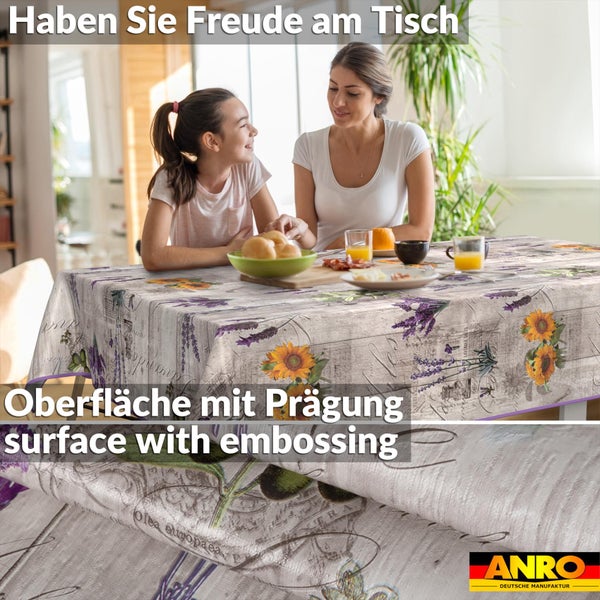 Abwaschbare Wachstuch-Tischdecke mit Sonnenblumen und Lavendel auf geprägter Oberfläche. Esszimmerszene. ANRO Deutsche Manufaktur Logo.