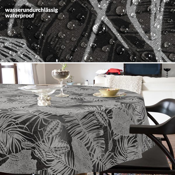Rundes Tischtuch in Schwarz und Grau mit tropischem Blattmuster auf einem Tisch im Wohnzimmer und Detail der wasserdichten Oberfläche.