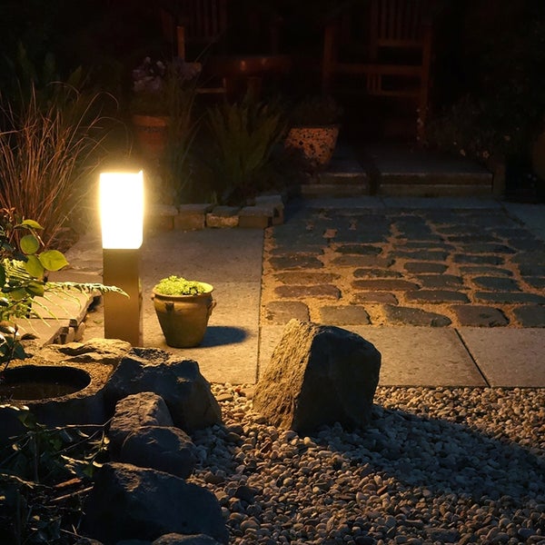 Moderne Garten-Standleuchte mit warmem Licht auf einer Steinterrasse bei Nacht.