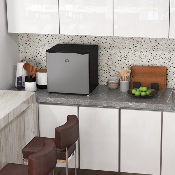 Moderne, helle Küche mit einem kompakten silbernen Mini-Kühlschrank auf einer grauen Steinarbeitsplatte, weißen Schränken und Terrazzo-Rückwand.
