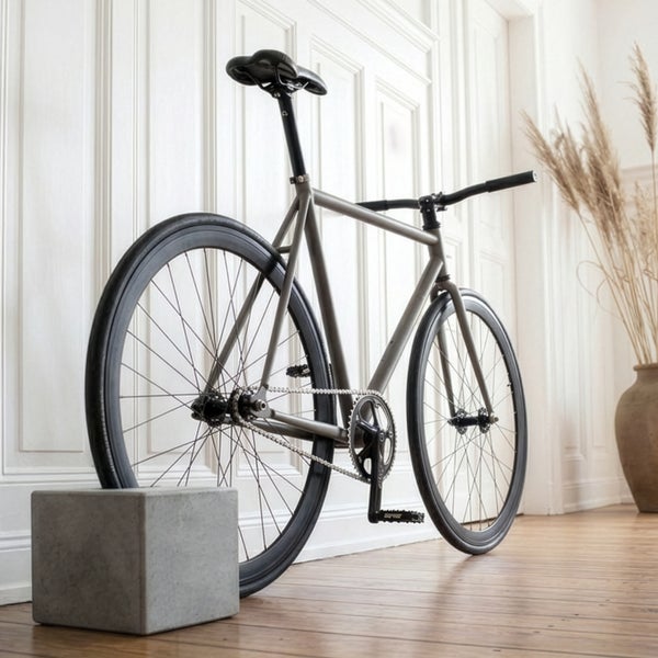 Modernes graues Fahrrad in einem hellen Raum mit weißen Wandpaneelen und Holzboden, gestützt von einem Betonwürfel.