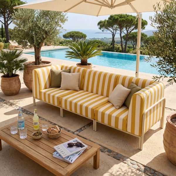 Heller Außenbereich mit gelb-weiß gestreiftem Sofa, Holz-Couchtisch und Pflanzen neben einem Pool.