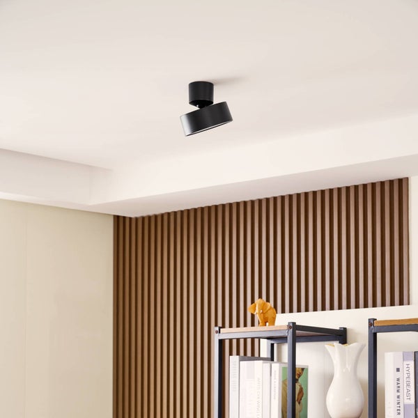 Schwarzer, verstellbarer Deckenstrahler an einer hellen Decke in einem modern eingerichteten Raum mit einer Wand aus Holzlamellen.