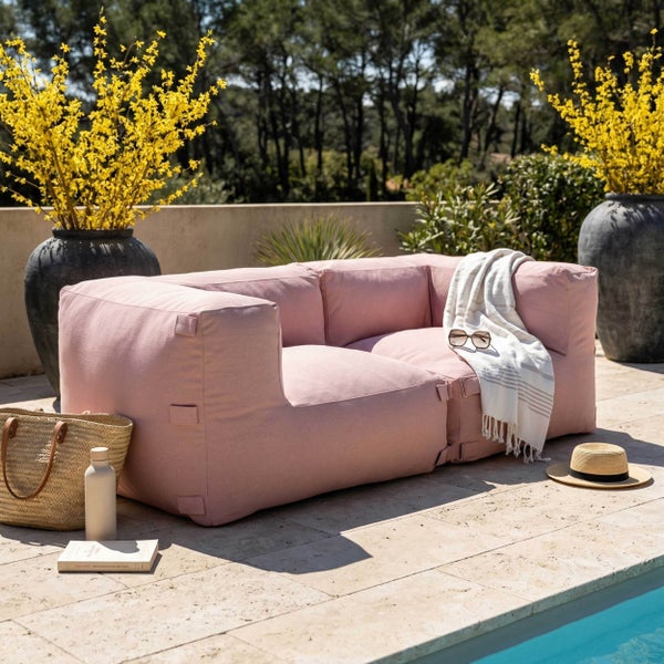 Modernes rosa Outdoor-Lounge-Sofa auf einer Steinterrasse am Pool, umgeben von großen Pflanzgefäßen mit gelben Blumen.