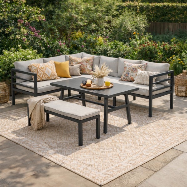 Garten-Lounge-Set mit Ecksofa, Tisch und Bank aus dunkelgrauem Metall, hellgraue Polster und gemusterte Kissen auf einem Außenteppich.