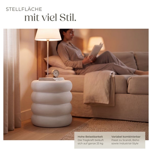 Runder Beistelltisch in organischer Form als Nachttisch neben einem Bett mit lesender Person, belastbar bis 25 Kilogramm.