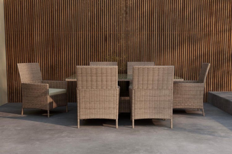 Gartenmöbel-Set bestehend aus einem Tisch mit Glasplatte und sechs Sesseln aus Polyrattan vor einer Wand aus Holzlamellen auf einer Terrasse.