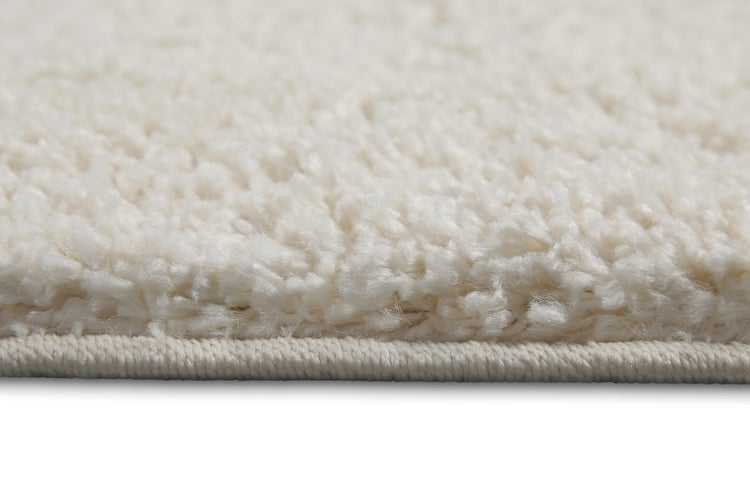 Detailaufnahme eines weißen Hochflor-Teppichs mit weichem Flor und geketteltem Rand.