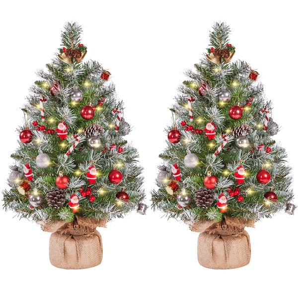 Zwei geschmückte Weihnachtsbäume mit Lichtern, Kugeln und Figuren auf einem Jutesack