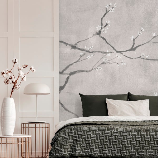 Schlafzimmer mit Wandtapete mit Kirschblütenmotiv hinter einem Bett mit gemustertem Tagesdecke und Kissen vor einer weißen Wandverkleidung.