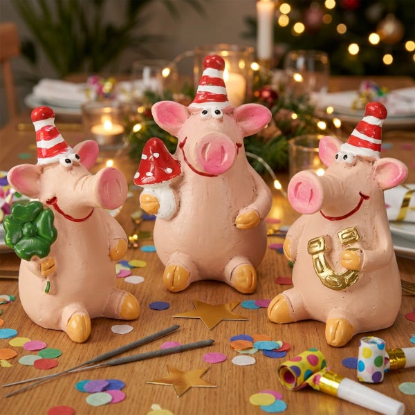 Drei dekorative Schweinchen als Glücksbringer für Silvester auf einem Tisch mit Konfetti und Partyzubehör.