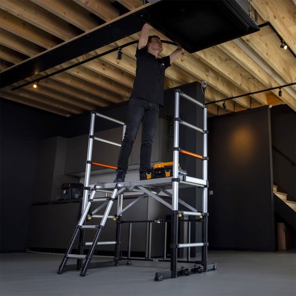 Eine Person arbeitet an einer Decke auf einem mobilen Aluminium-Plattformgerüst mit Sicherheitsgeländer und Leiteraufstieg.