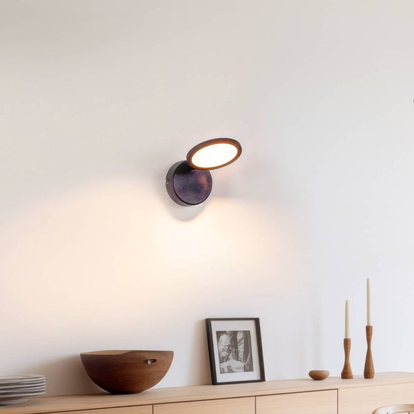 Schwarze LED-Wandleuchte mit kreisförmigem, schwenkbarem Kopf über einem Sideboard aus hellem Holz.