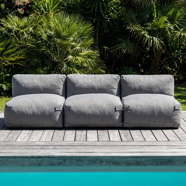 Dreisitzer-Modul-Gartenlounge in Grau auf einer Holzterrasse am Pool mit tropischen Pflanzen im Hintergrund.