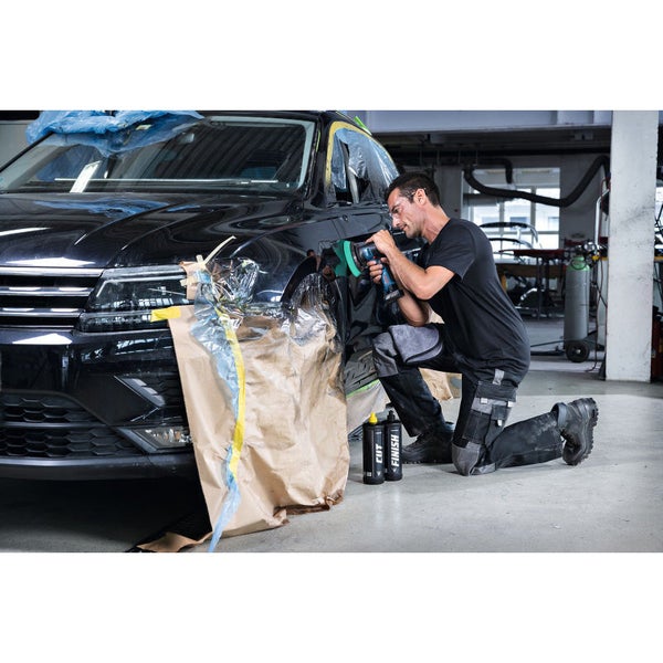 Ein Mann poliert ein Auto mit einer Poliermaschine. Zwei Flaschen mit Schleifpolitur stehen daneben.