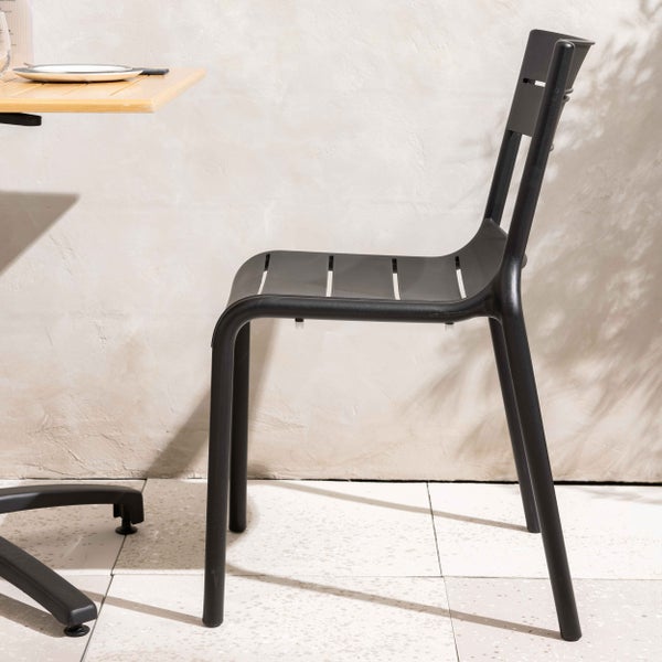 Moderner Gartenstuhl aus schwarzem Metall mit Sitzfläche und Rückenlehne aus Lamellen, Seitenansicht neben einem Tisch.