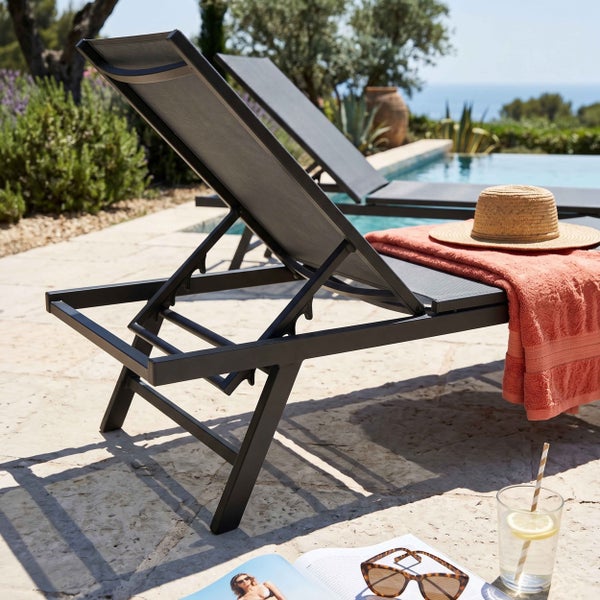 Verstellbare Gartenliege aus Metall mit Textilbespannung auf einer hellen Steinterrasse am Pool mit sommerlichen Accessoires.