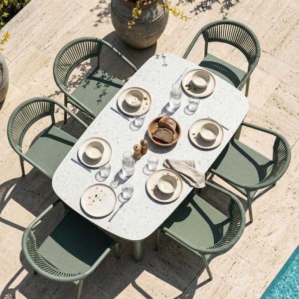 Modernes Garten-Set mit ovalem Tisch in Terrazzo-Optik und sechs grünen Gartenstühlen mit Seilgeflecht auf einer hellen Steinterrasse.
