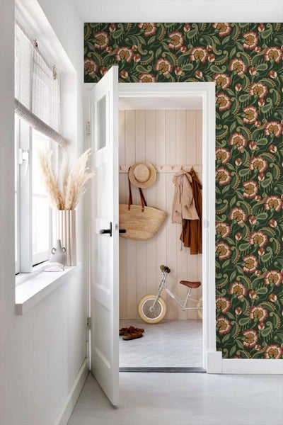 Heller Flur mit floral gemusterter Tapete, offene Tür führt in einen Raum mit Holzpaneelen, Kinderlaufrad und Strohtasche.