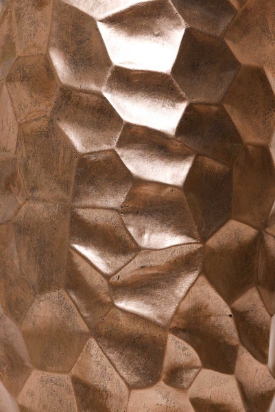 Detailansicht einer gehämmerten Metalloberfläche mit geometrischem Facettenmuster in Bronzeoptik.