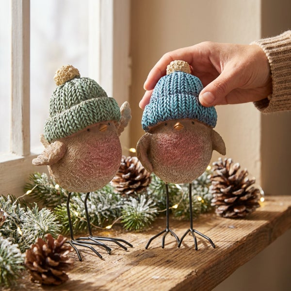 Zwei dekorative Vogel-Figuren mit Mützen als Winter-Weihnachtsdekoration auf einem Holzbrett mit Tannenzweigen und Tannenzapfen.