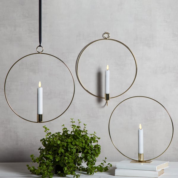 Dekorative Szene mit drei goldenen Kerzenhaltern mit Kerzen, Pflanze und Büchern.