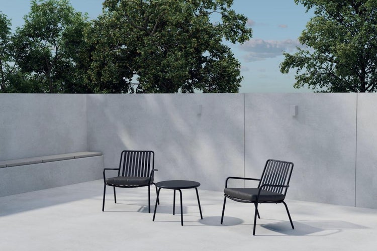 Modernes Gartenmöbel-Set bestehend aus zwei Sesseln und einem runden Tisch auf einer Betonterrasse vor einer Mauer und Bäumen.