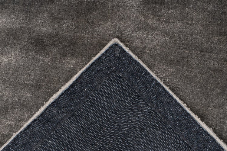 Nahaufnahme eines dunkelgrauen Teppichs mit umgeknickter Ecke, weiche Oberseite und strukturierte Unterseite mit verstärktem Rand.