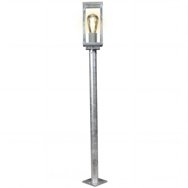 Moderne Wegeleuchte aus verzinktem Stahl mit rechteckigem Glaskopf und sichtbarem Leuchtmittel auf einem hohen Standrohr.