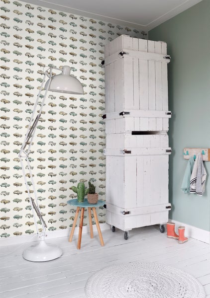 Helles Zimmer mit Oldtimer-Tapete, weißer Stehlampe, Holzhocker mit Kakteen, weißem Holzschrank und rundem Teppich