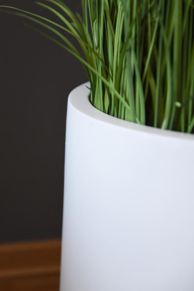 Detailaufnahme eines künstlichen Grases in einem weißen zylindrischen Blumentopf.