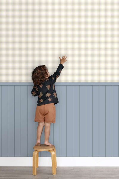 Kind steht auf einem Hocker vor einer Wand mit karierter Tapete und vertikalen Wandpaneelen im Kinderzimmer.