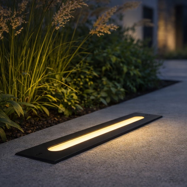 Moderne LED Bodeneinbauleuchte für den Außenbereich entlang eines Gartenwegs mit Ziergräsern.
