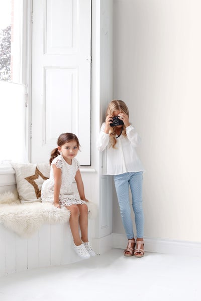 Helles Zimmer mit zwei Mädchen, eines mit Kamera, das andere sitzt auf einer Bank mit Kissen