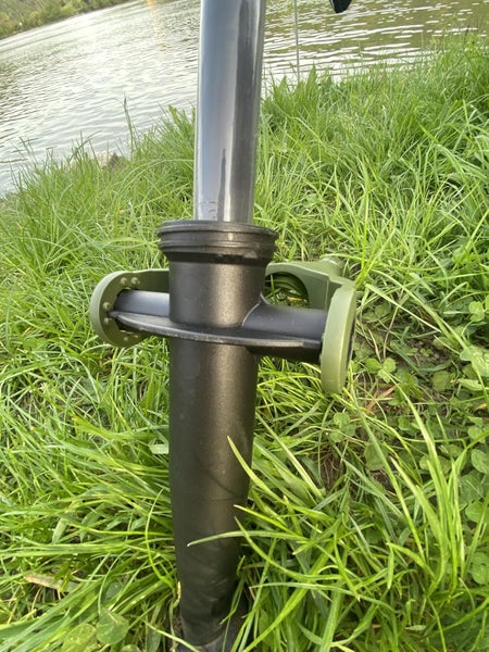 Bodendübel aus schwarzem Kunststoff für Sonnenschirme, im grünen Gras am Wasserufer mit eingesetztem Mast.