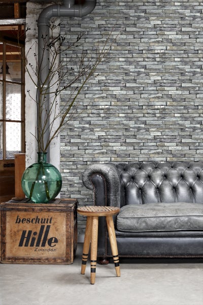 Wohnzimmer mit Steinwandtapete, Ledersofa und Holzhocker