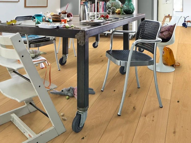Parkettboden in Eichenoptik in einem Esszimmer mit metallenem Tisch auf Rollen und verschiedenen Stühlen.