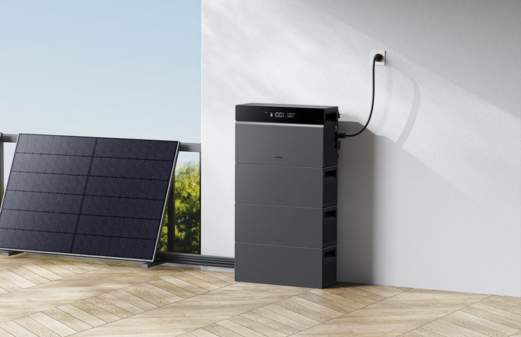 Balkonkraftwerk mit Solarmodul und stapelbarem Speicher mit Display, angeschlossen an eine Außensteckdose auf einer hellen Terrasse mit Holzboden.