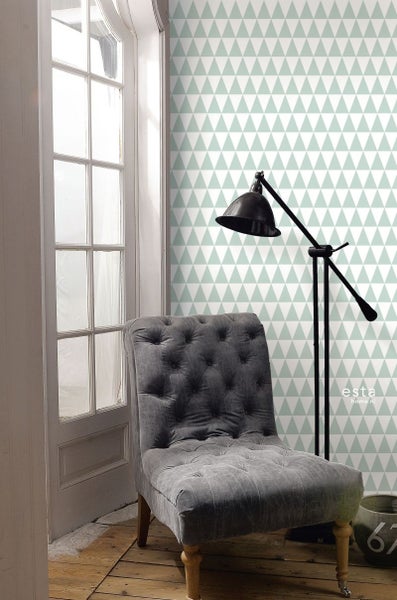 Vliestapete mit geometrischem Dreiecksmuster in einem hellen Raum mit gepolstertem Sessel, schwarzer Stehlampe und weißer Sprossentür.