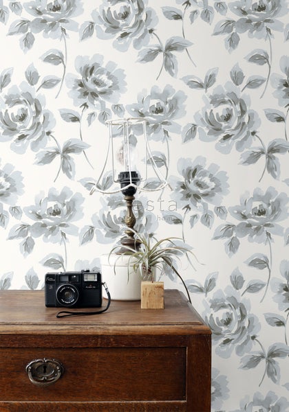 Szene mit einer Kommode, einer Lampe, einer Zimmerpflanze, einer Kamera und einer Tapete mit Blumenmuster