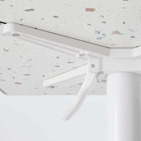 Detailaufnahme der Unterseite eines Tisches mit einer Tischplatte in Terrazzo-Optik und einem weißen Klappmechanismus aus Metall.