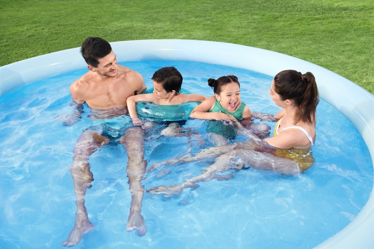 Familie mit zwei Kindern entspannt in einem runden aufblasbaren Pool im Garten auf einer Rasenfläche.