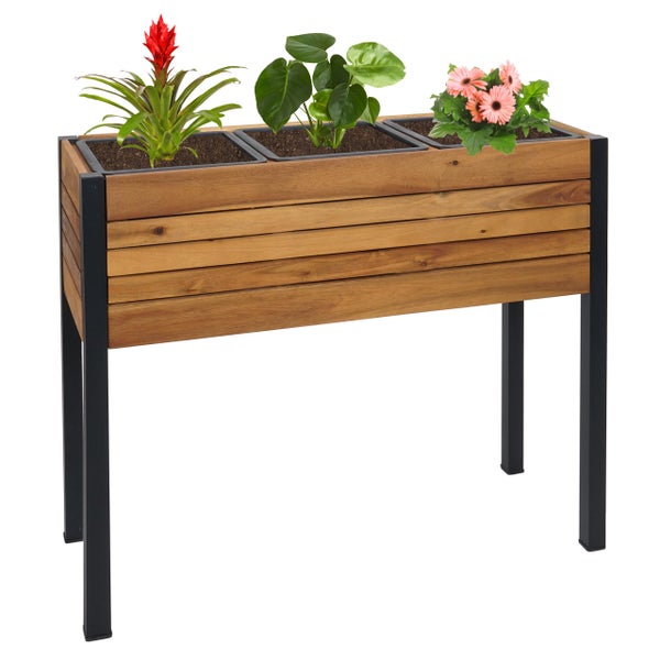 Hochbeet aus Holzlamellen mit schwarzen Metallbeinen und drei Pflanzeinsätzen, bepflanzt mit Blumen und Grünpflanzen.