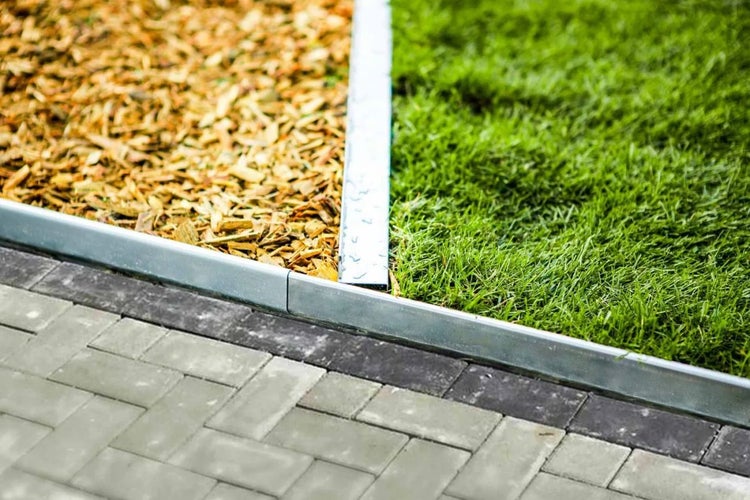 Beeteinfassung aus Metall trennt Rasen, Rindenmulch und Pflastersteine