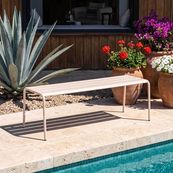 Moderne Gartenbank aus Metall auf einer Steinterrasse am Pool, umgeben von einer Agave und Tontöpfen mit bunten Blumen.