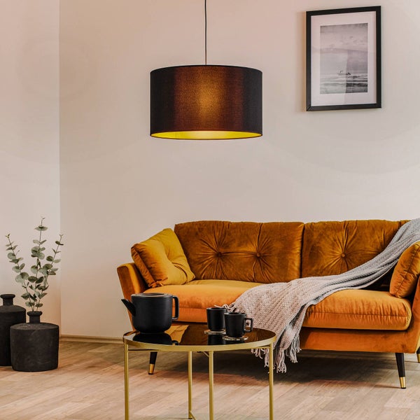 Moderner Wohnraum mit gelbem Samtsofa, schwarzer Pendelleuchte mit goldener Innenseite und rundem Metall-Couchtisch.