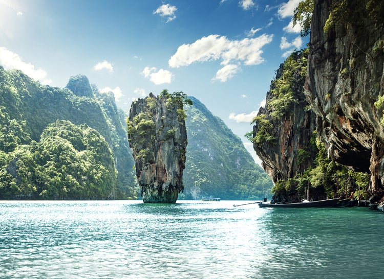 Fototapete einer tropischen Bucht in Thailand mit steilen Kalksteinfelsen im Meer und einem Boot am Ufer bei sonnigem Wetter.