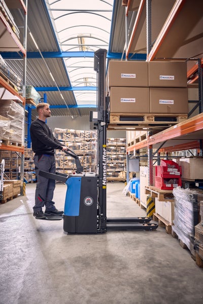 Ein Mitarbeiter bedient einen elektrischen Hochhubwagen von HanseLifter im Lager und hebt eine Palette mit Kartons an.