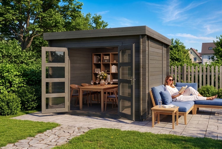 Modernes Gartenhaus aus Holz mit Flachdach und Doppeltür mit Glaseinsätzen, davor eine Terrasse mit Loungemöbeln und einer Frau beim Lesen.